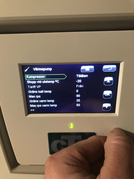 Digital kontrollpanel för värmepump, hand justerar inställningar, blå bakgrundsbelysning, text och symboler på svenska.