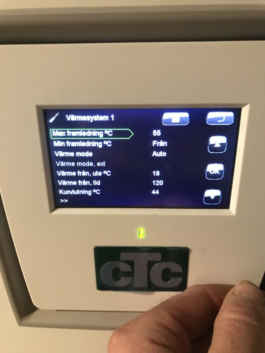 Digital termostat för värmesystem visar inställningar och temperaturvärden. En hand justerar inställningarna.