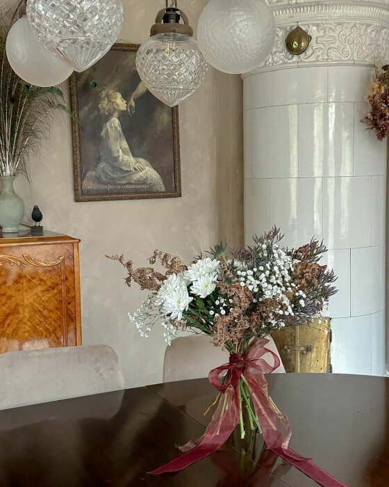 Klassiskt inrett rum med blommor, konstverk, taklampor och antik möbel.