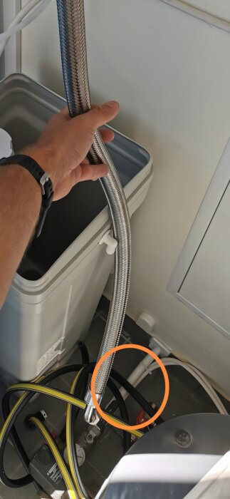 Hand som håller vattenslang vid tvättmaskin, med cirkelmarkerad detalj som kan vara problematisk.