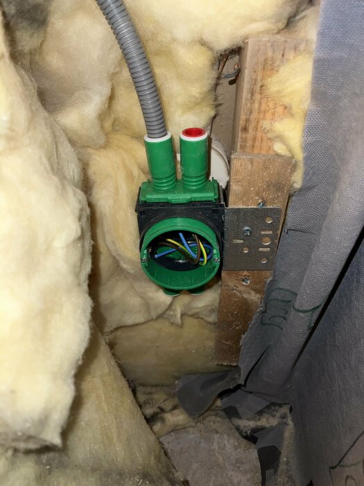 Eluttag under installation, omgiven av isolering och kablar, i en väggkonstruktion.