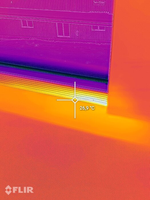Termisk bild visar värmevariationer, yttemperatur 26,9 °C, möjlig isoleringskontroll av byggnad.