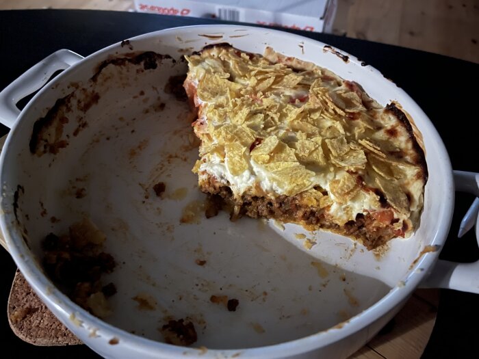 Uppäten lasagne i vit ugnsform med några kvarvarande bitar och potatischips på toppen.