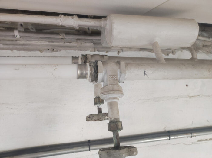 Vitmålade rör och ventiler på en betongvägg, installationsdetaljer, inomhus VVS-system.