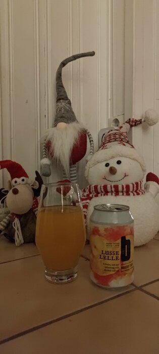 En tomte, snögubbe, apa, glas med dryck och dryckesburk på bänk med en julstämning.