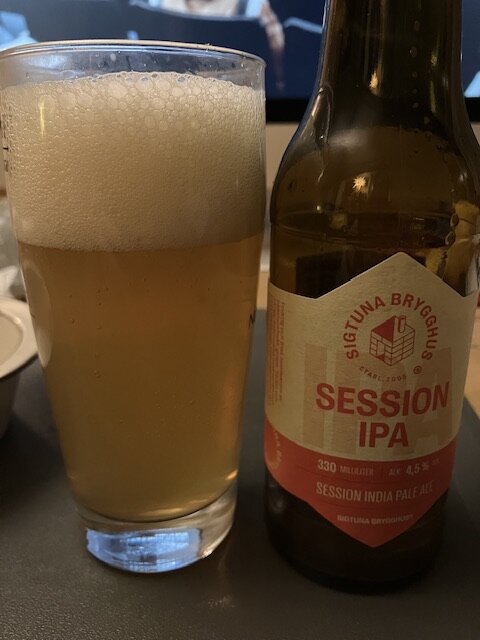 Ett glas ljus öl bredvid en tom ölflaska märkt "Session IPA".