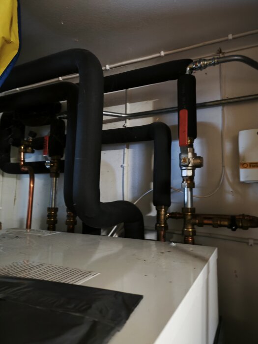 Värmesystem med isolerade rör ovanför en vit apparat, tekniska installationer, reglage och ventiler, inomhusmiljö.