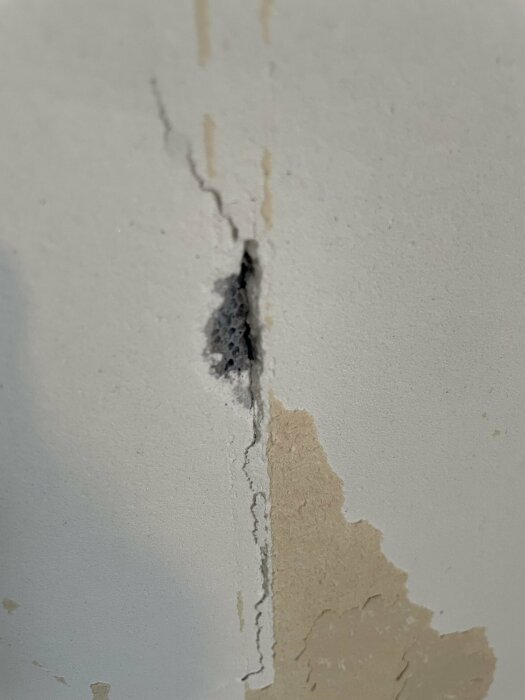 Skadad vägg med spricka, flagande färg och möjlig vätskemarkering.