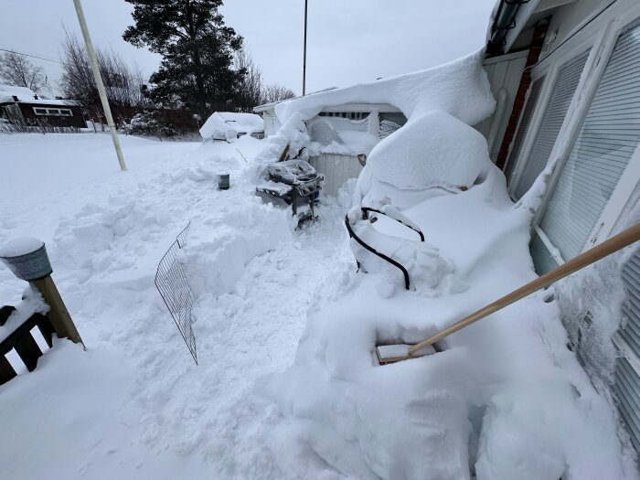 Terrass och grill täckt av tjockt snötäcke; skottad gång; vinter; dagtid; trädgårdsmöbler begraven i snö.