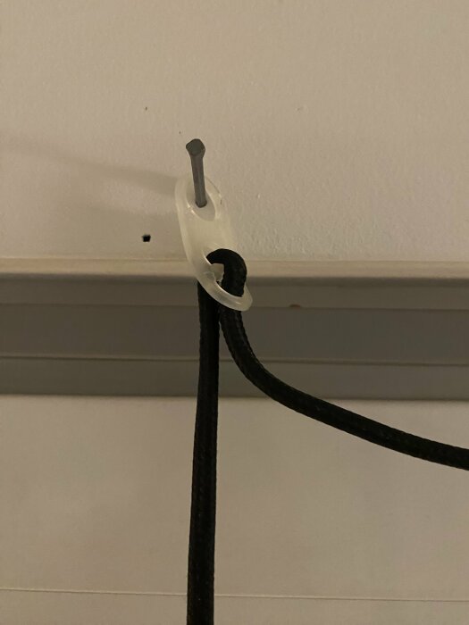 Vit kabelklämma håller en svart kabel mot en vit vägg över en golvlist.