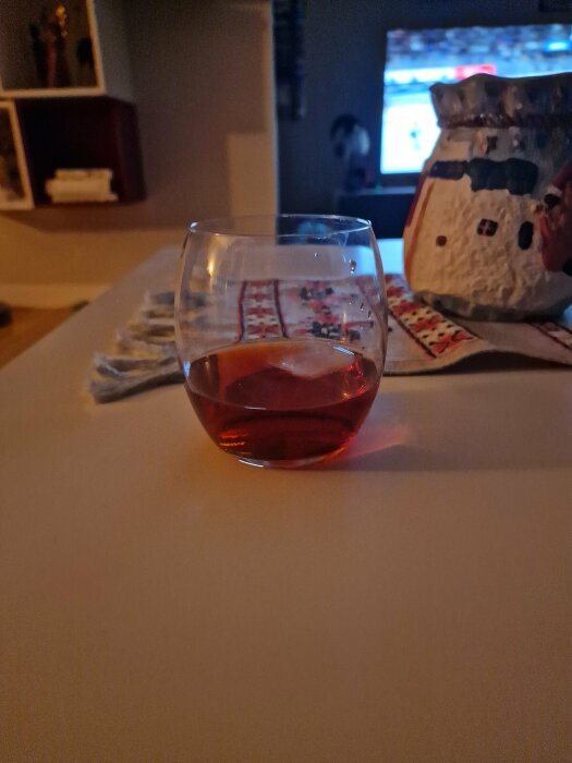 Ett glas rosévin i förgrunden, mysig stämning med suddig TV och inredning i bakgrunden.