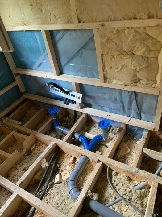 Renoveringsarbete pågår, isolering och vattenrör synliga i träbjälklag, byggmaterial, oavslutade inomhuskonstruktioner.