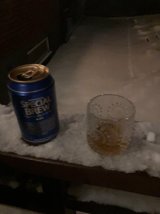 Burk Special Brew och ett glas på ett snötäckt bord utomhus på kvällen.