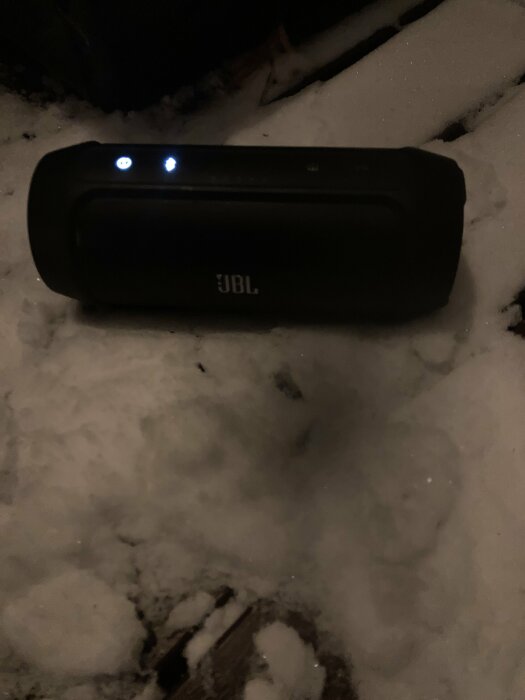 Bärbar högtalare från JBL på nattlig snöyta med tända indikatorlampor.