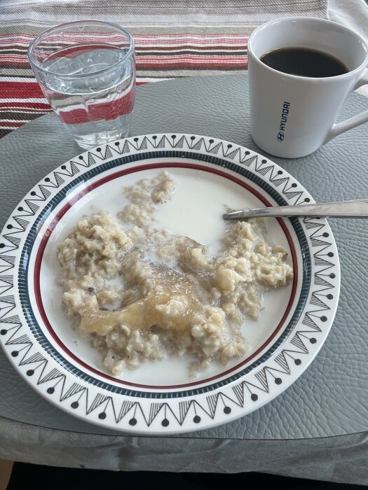 Havregrynsgröt med sylt på tallrik, kaffe och vatten, mönstrad bordsduk, enkelt frukostarrangemang.