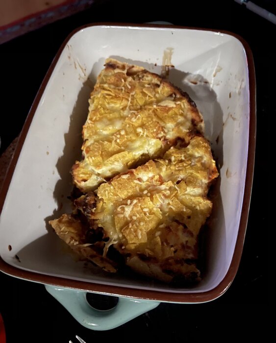 En ugnsform med en serverad portion av en potatisbaserad maträtt, möjligen potatisgratäng, med ost på toppen.