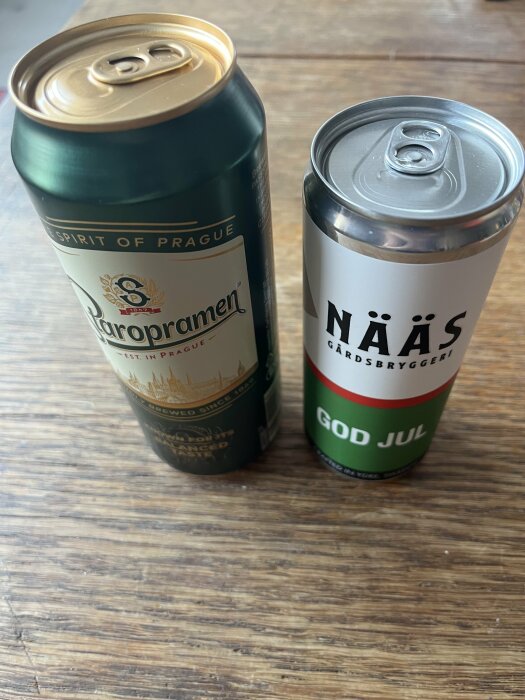 Två ölburkar på träbord: en stor Staropramen och en liten Nääs med "God Jul"-tema.