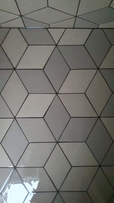 Mönstrat kakelgolv i grått med hexagonala plattor, spegelningar och skuggor, samt ett litet vattenpöl.