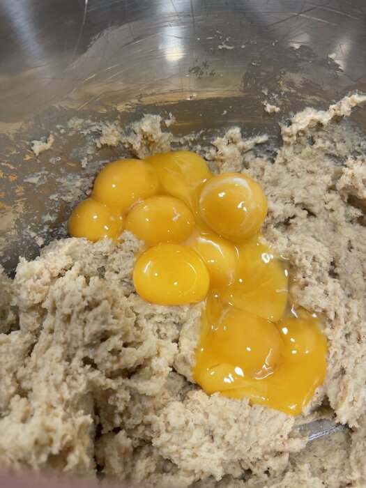 Sju äggulor på obakad deg i metallskål. Matlagning, ingredienser, bakning, kök.