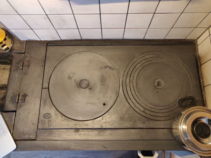 Gammaldags vedspis i gjutjärn med kokplattor och ugn, placerad i ett kök.