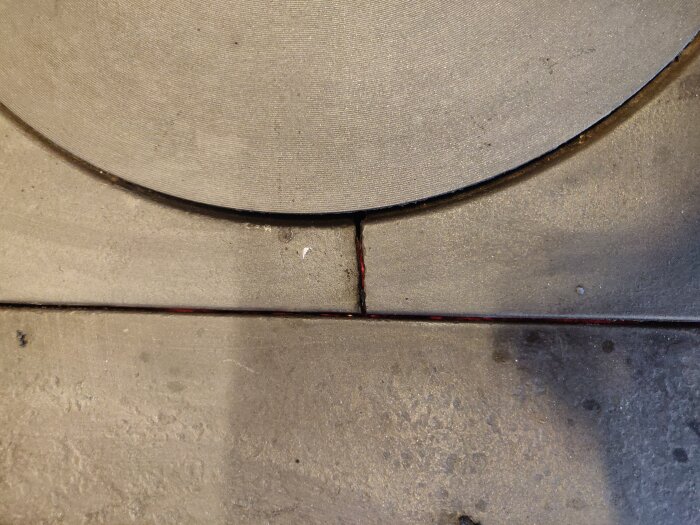 Textilhalvcirkel över betonggolv: möter stenplattor med röda foglinjer. Slitna, grova ytor. Subtil färgkontrast, enkel komposition.