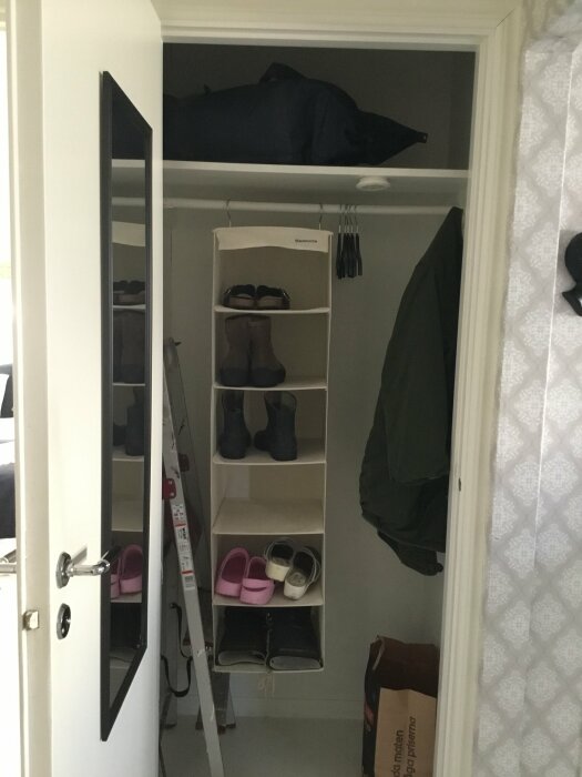 Öppen garderob med hyllor, skor, kläder, dörr med spegel, inomhusmiljö.
