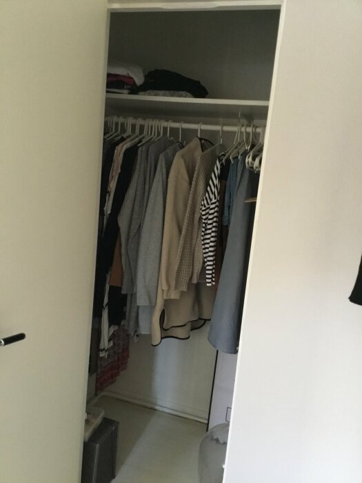 En öppen garderob med kläder på galgar och hyllor, neutralt färgschema, hemmamiljö.