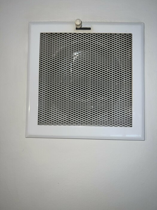Väggmonterad ventilationsgrill i vit ram med clip, på en vit vägg.