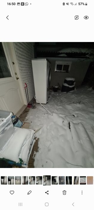 Kylskåp och frys utomhus i snö vid ett hus under kvällen.