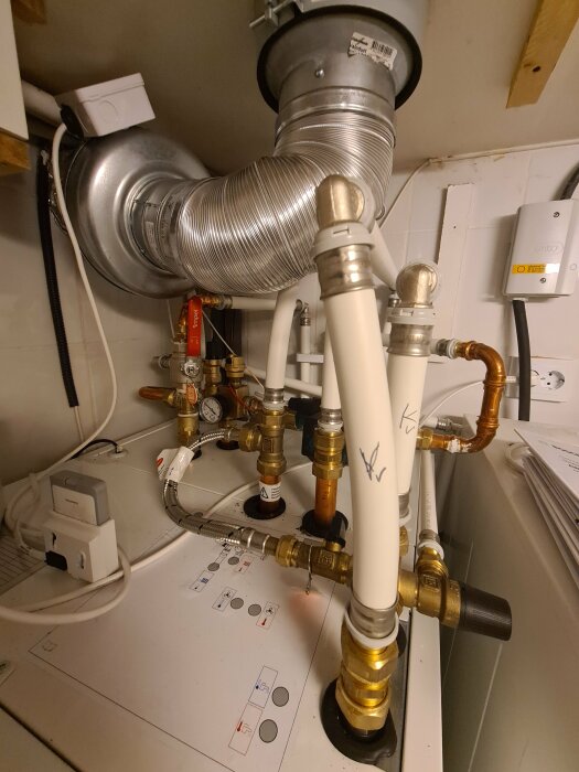 Rörsystem och elinstallationer under en diskbänk, ventilation, vattenledningar och säkerhetsbrytare synliga.