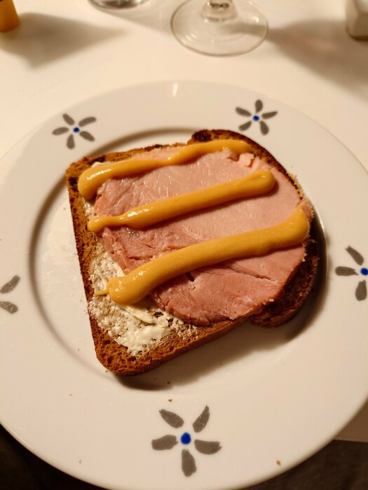 Rostat bröd med skinka, senap och smörgåskryddning på en dekorerad tallrik.