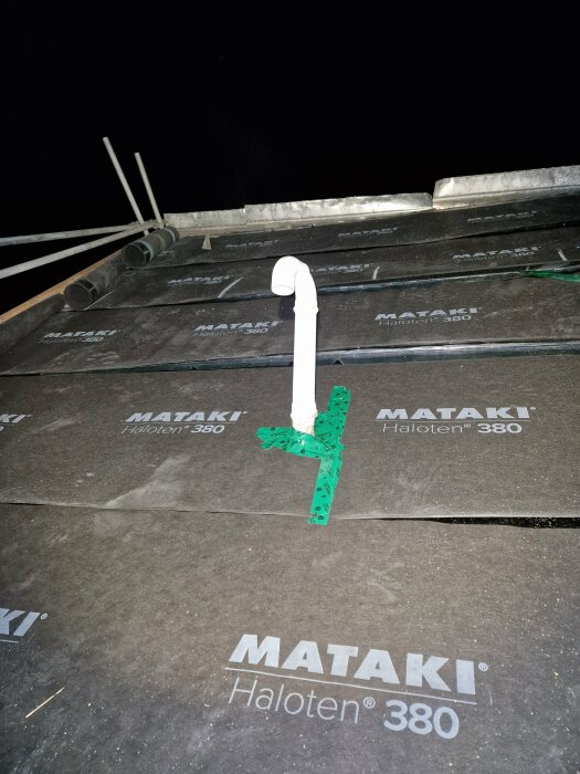 Tak med avloppsrör, tätskikt, märkt "MATAKI Haloten 380", mörk bakgrund, rör fastsatt med grön tejp.