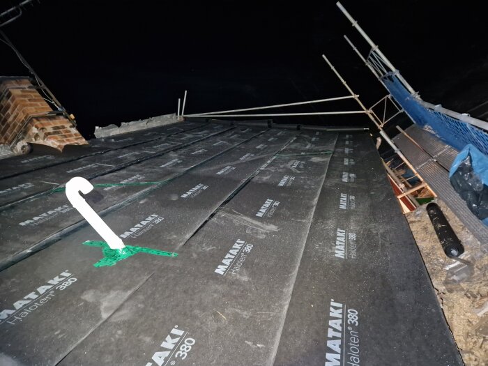 Nedre del av ett tak under konstruktion på natten med brandskyddsfilt och byggställning synlig.
