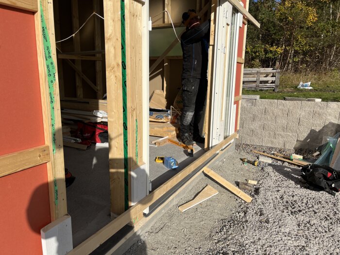 Arbetsplats utomhus, byggarbetare installerar fönster, trästomme, verktyg och byggmaterial spridda, dagtid.