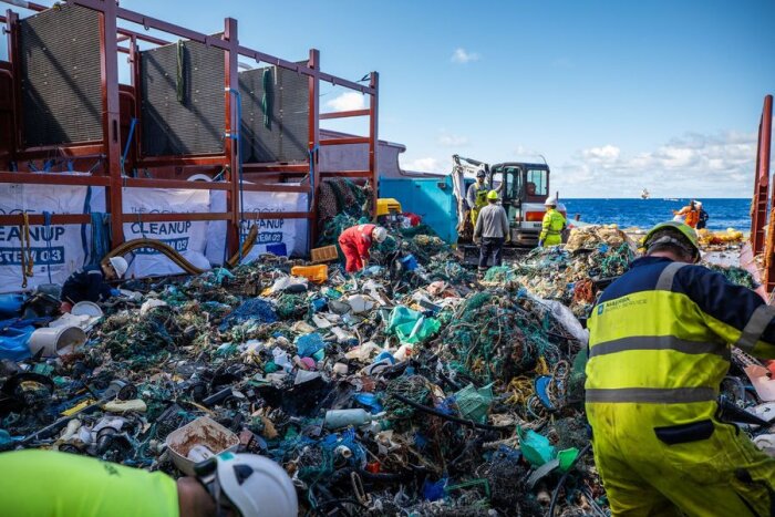 Sjörensning av plast, arbetare sorterar avfall på skeppsdäck, miljöarbetet syns, havet i bakgrunden.