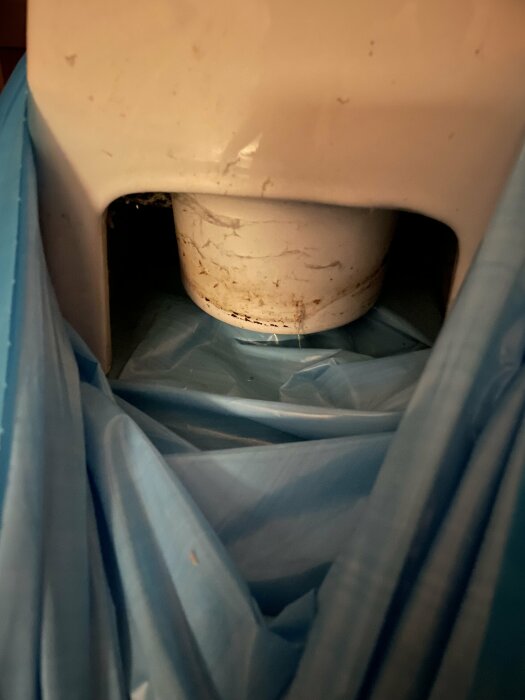 Toalettstol fotograferad uppifrån, nedre del synlig, i en soptunna med blå soppåse.