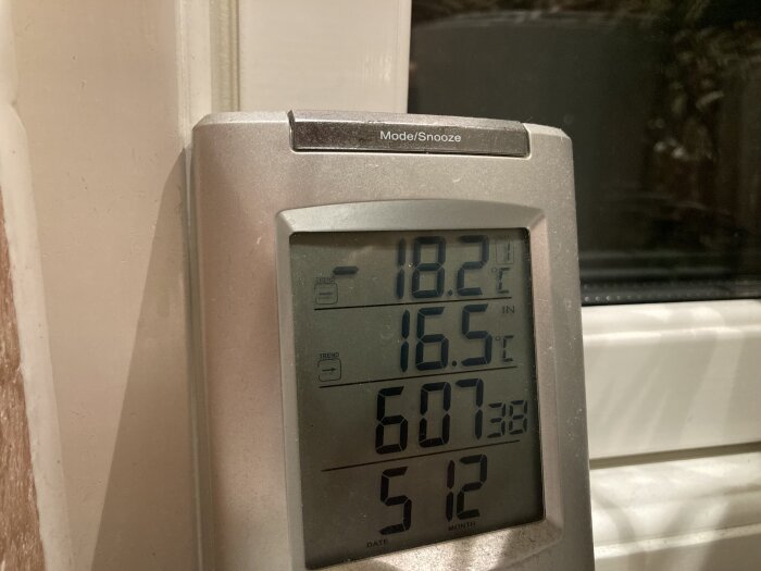 Digital termometer inomhus och utomhus temperaturvisning, datum och tid, nära ett fönster.