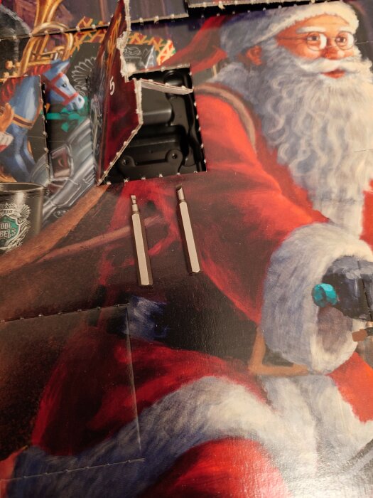 Julkalender med öppnad lucka, bild av tomte, brun häst syns delvis, två vita tändstickor framför.
