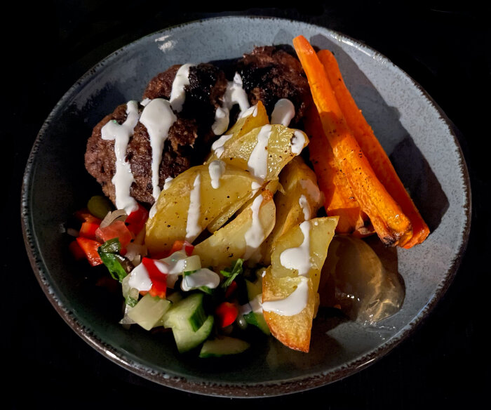 En tallrik med biff, ugnsrostade morötter, kryddade potatisar och färsk grönsakssallad, drizzled med sås.