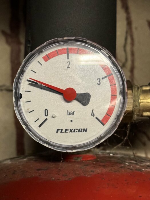 Manometer med röd svart skala, märkt "FLEXCON", visar tryck under 1 bar, lite dammigt.