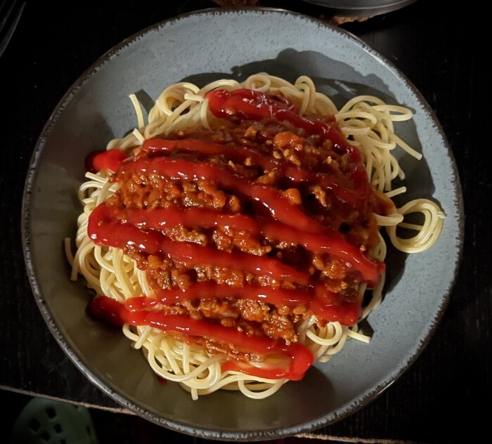 Spaghetti med köttfärssås och rikligt med ketchup på en tallrik. Kvällsmåltid eller middag.