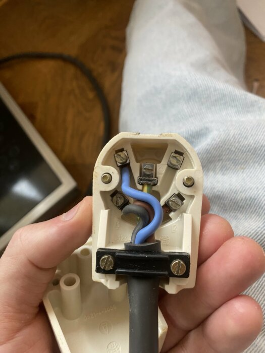 En person håller en öppen elektrisk kontakt med blå och bruna sladdar synliga. Reparation eller inspektion pågår möjligen.
