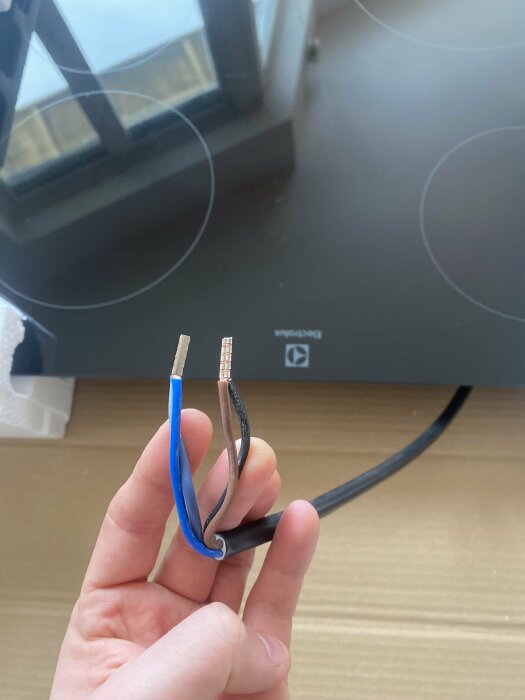 En hand håller avskalade ändar av en avklippt elektrisk kabel över ett bord.