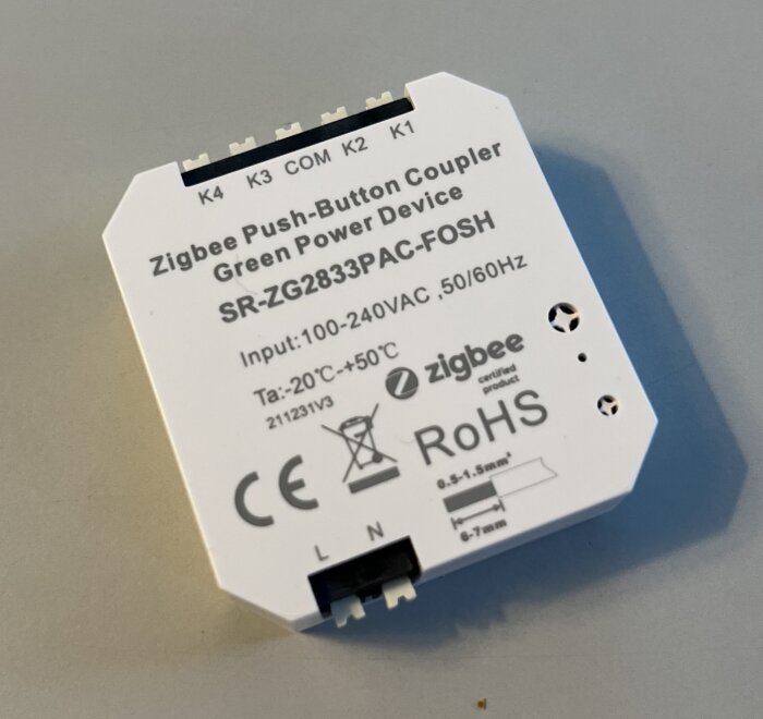 En Zigbee Push-Button Coupler, smart enhet, elektrisk komponent, vit bakgrund, tekniska specifikationer, anslutningsterminaler, säkerhetsmärkningar.