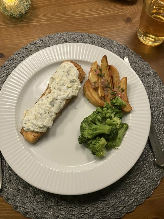 Middagstallrik med lax, dill-sås, rostad potatis, broccoli, på träbord.