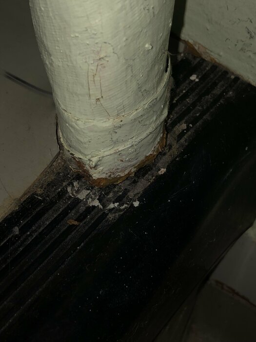 Vit målad rörstam med flagnande färg och rost nära mörk bas och golv.