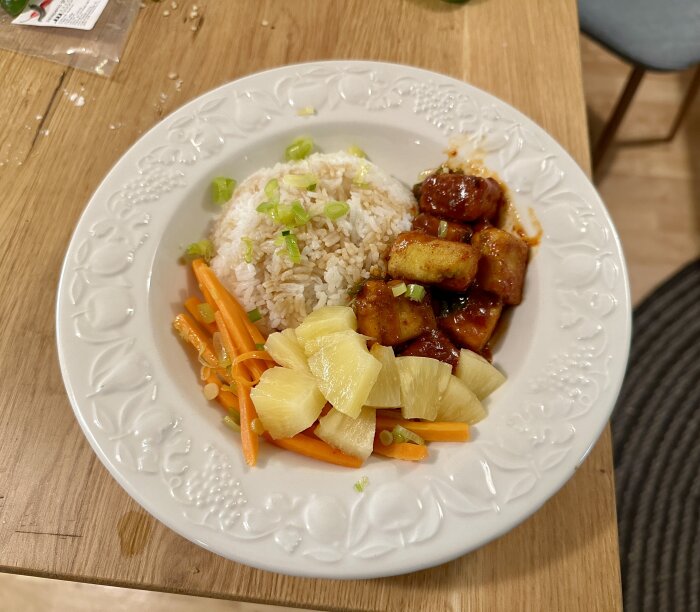 Ett måltid med ris, sötsur sås, ananas, morötter och tofu på dekorerad tallrik.