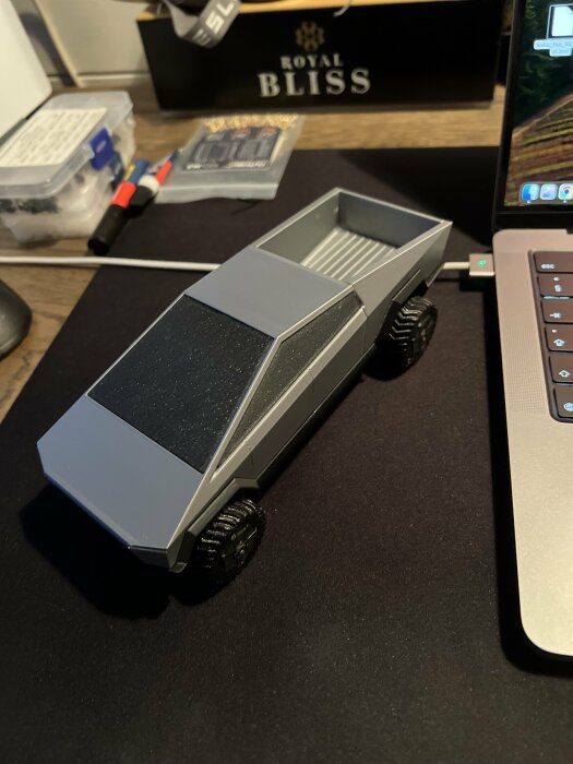 En modell av en pickup-truck med futuristisk design på ett skrivbord, intill en laptop.