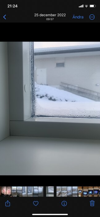 Fönster med isbildning, snö utanför, grå himmel, interiör av vitt rum, vinterdag.