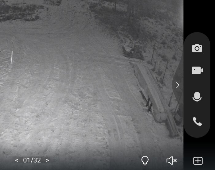 Övervakningskamera vy över snötäckt område med parkbänkar och träd, nattbild.